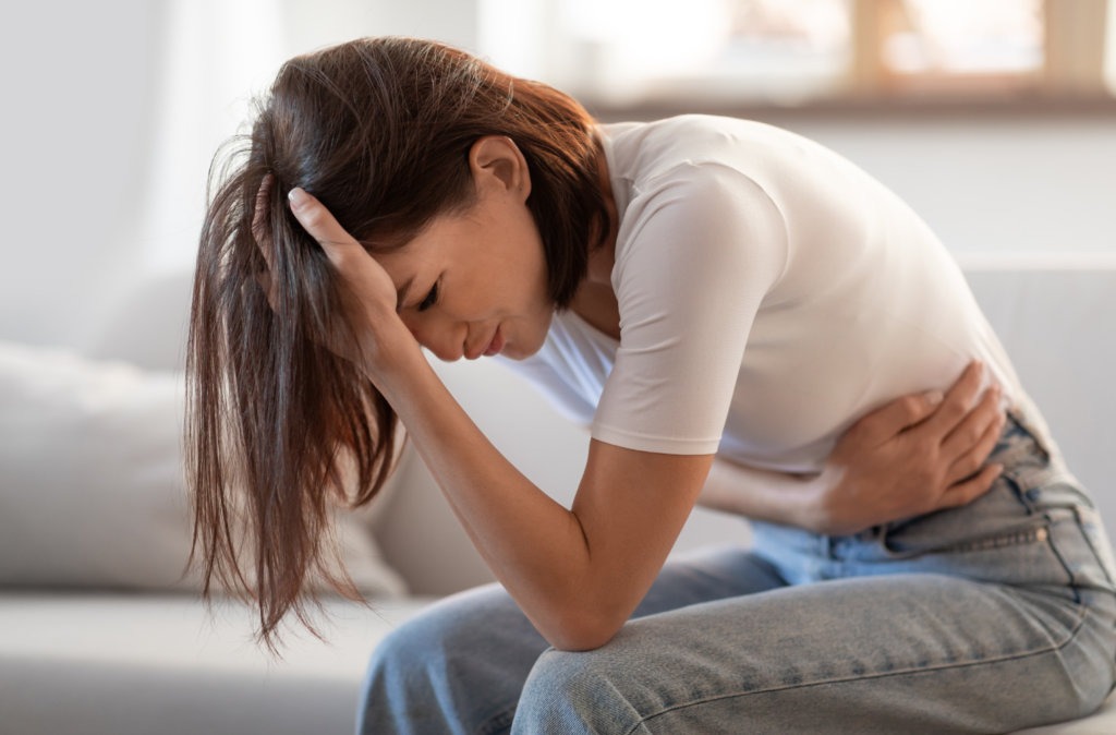 Mulher jovem com dor pélvica segurando o estômago – possível sintoma de endometriose