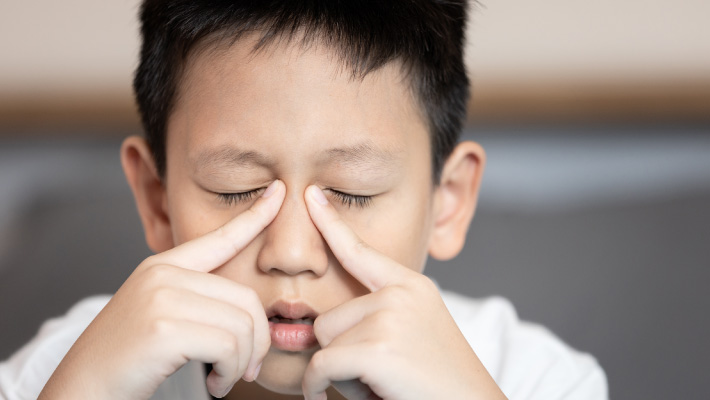 Menino com rinite coçando os olhos devido a alergia.