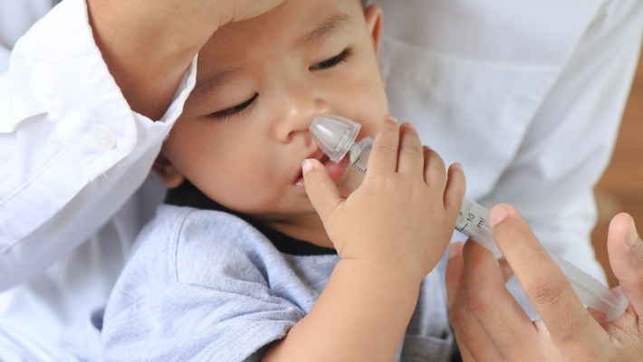 Mãe a fazer lavagem nasal no bebé para aliviar congestão nasal e melhorar a respiração.
