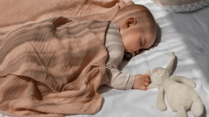 Bebé a dormir profundamente no berço com uma manta rosa, num ambiente calmo.