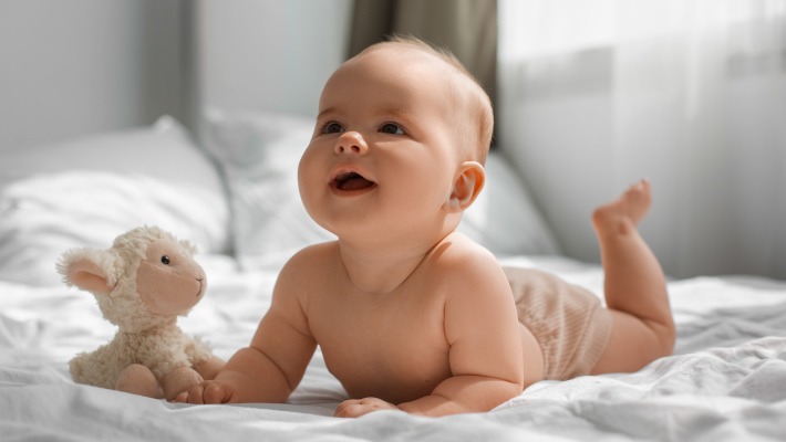 Bebé deitado de bruços, a sorrir, após um sono reparador.