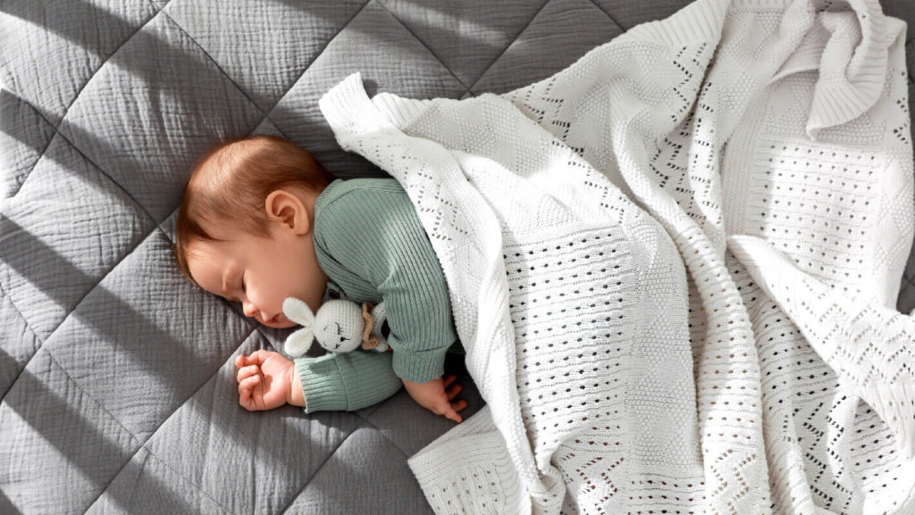 Bebé a dormir no berço, coberto com uma manta de malha.